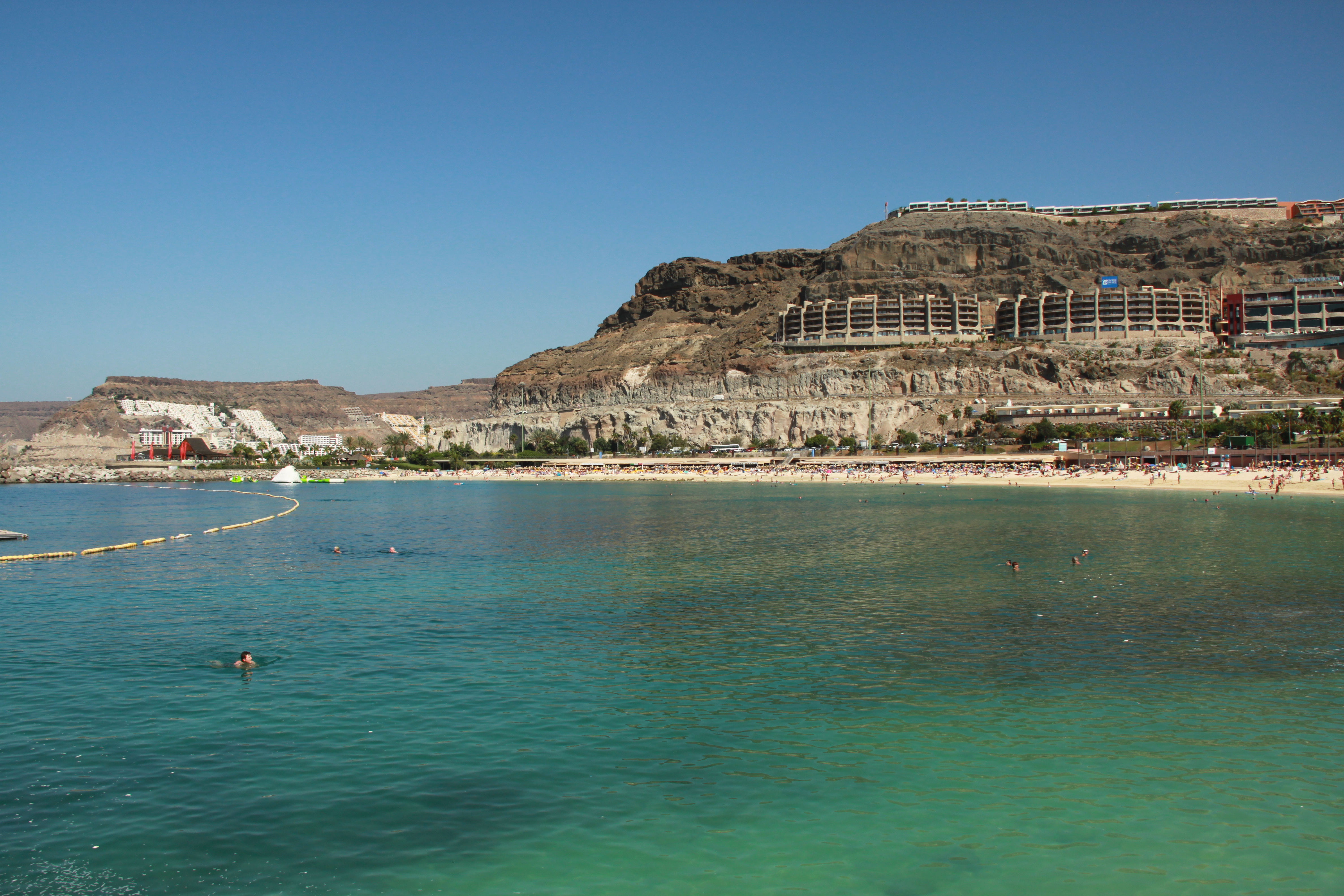 Sunny beach resort with turquoise sea, swimmers, and terraced cliffside buildings